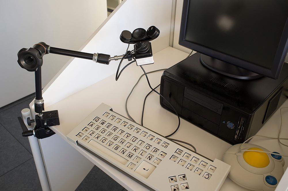 Adaptive computer setup for a user with impairments, featuring a specialized keyboard, mouse, and mounted camera for accessibility.