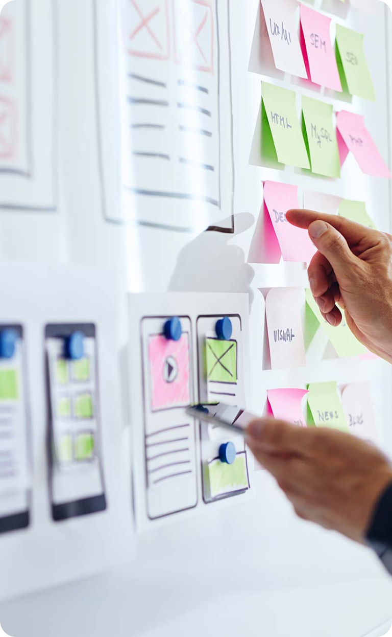 Close-up of a hand pointing at a whiteboard with mobile app interface sketches and colorful sticky notes for project planning.