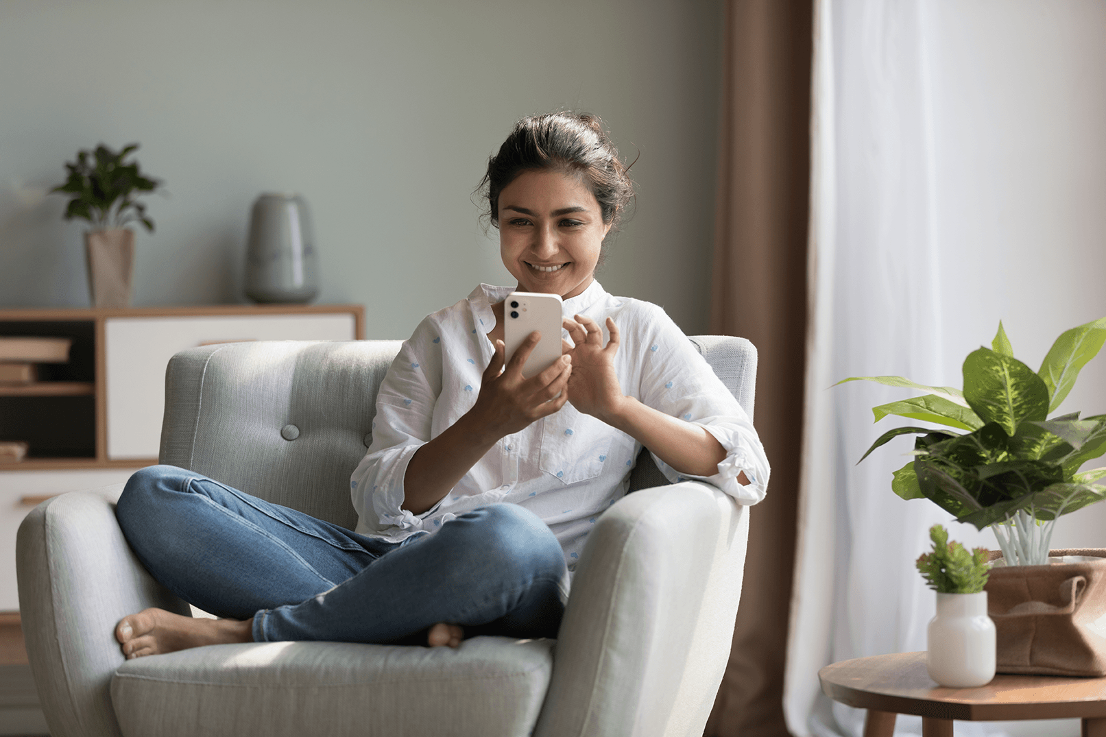 Woman sitting comfortably on a chair while smiling and using her phone.