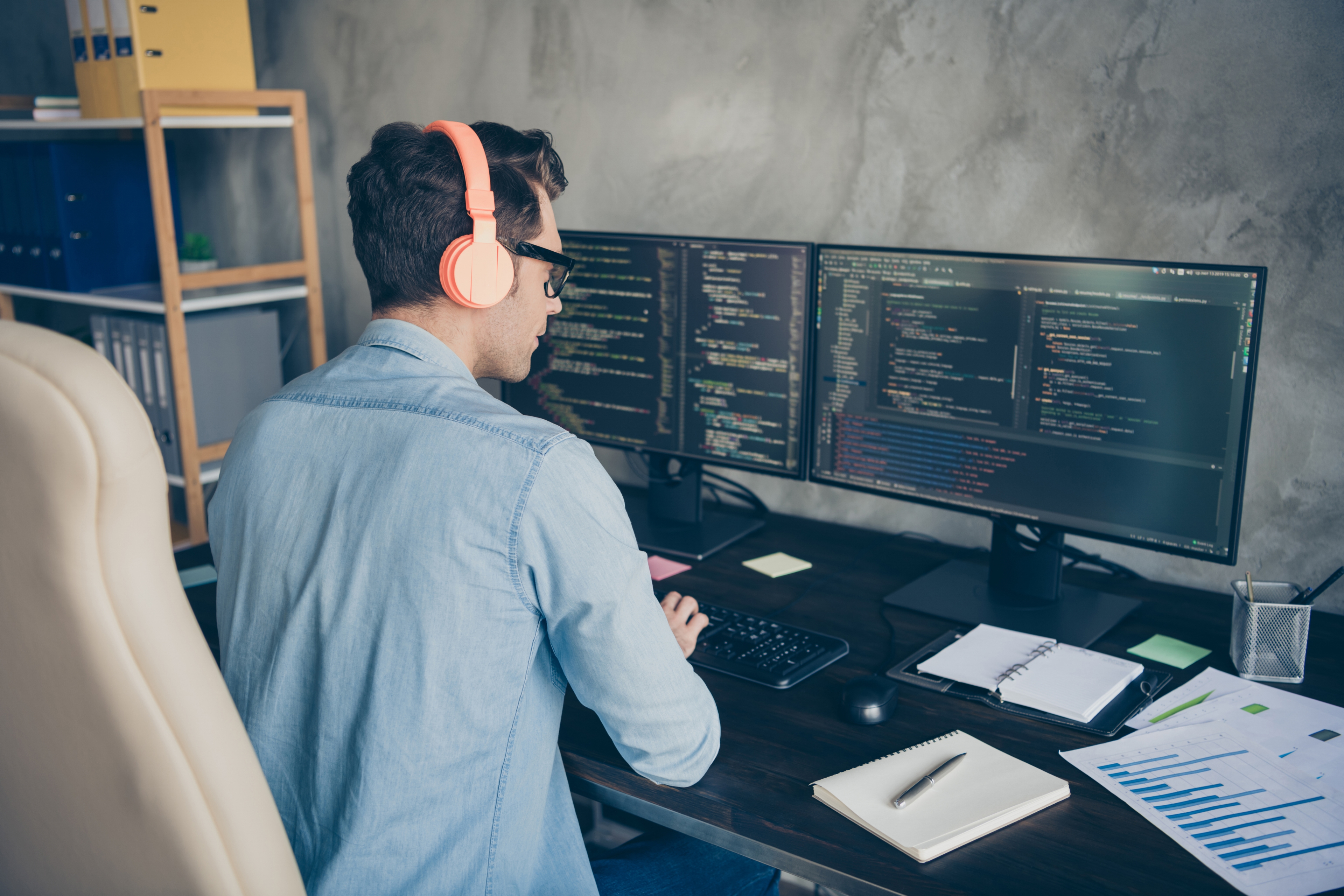 A developer coding with headphones on, focused on two monitors