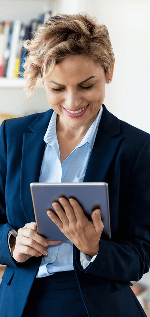 Professional woman with short curly hair smiling while looking at a digital tablet in her hand, dressed in a business suit.