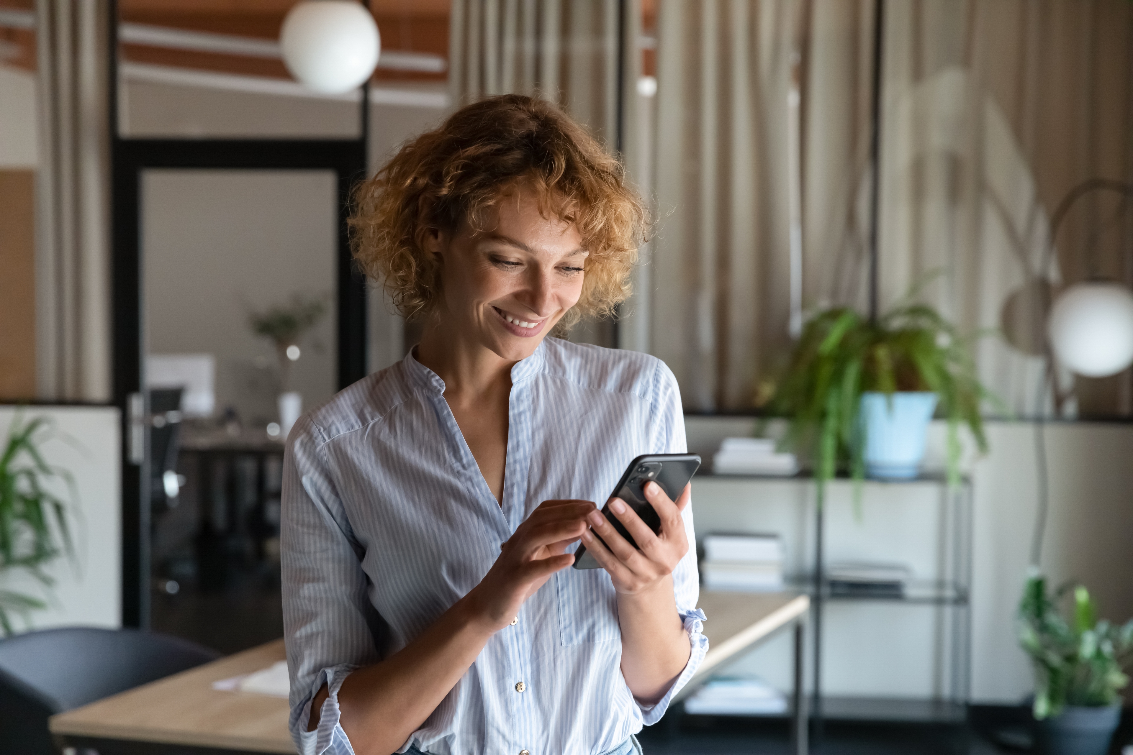 Smiling woman checking messages on her phone in a modern office.