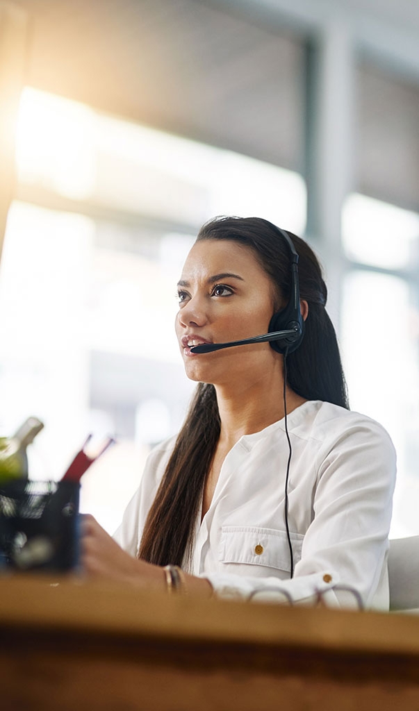 Woman with headset at a desk, assisting a customer in a bright, professional setting.