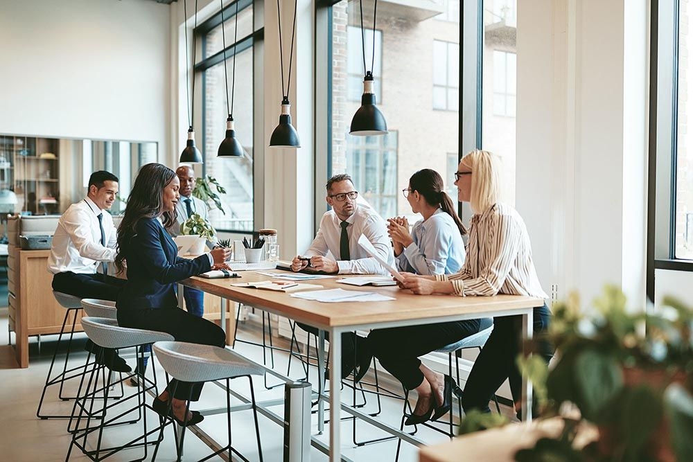 Startup team having a group meeting in a modern office with large windows and hanging lights.