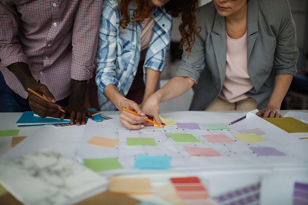 Diverse team collaborating on a project, reviewing and discussing a large document with colorful sticky notes on a table.