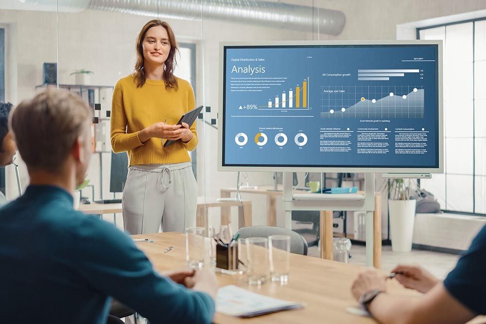 Businesswoman presenting a growth analysis report with charts and graphs on a large screen to colleagues in a modern office meeting room.