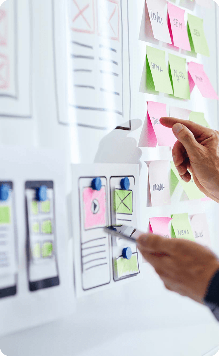 A hand pointing at a whiteboard with app interface sketches and  sticky notes for project planning.